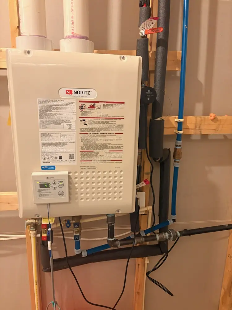 Noritz tankless water heater mounted on a wall with gas and water connections
