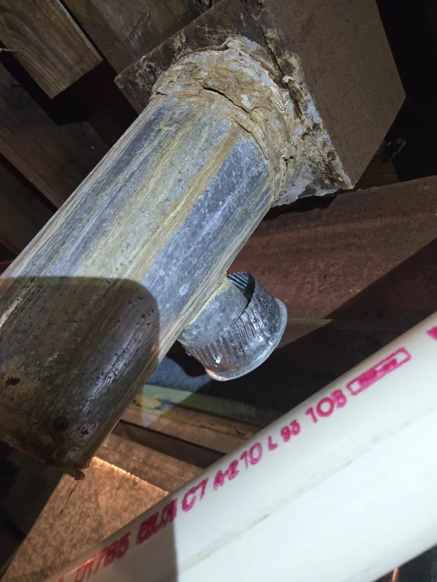 Old corroded metal flue pipe entering a chimney thimble in a basement ceiling