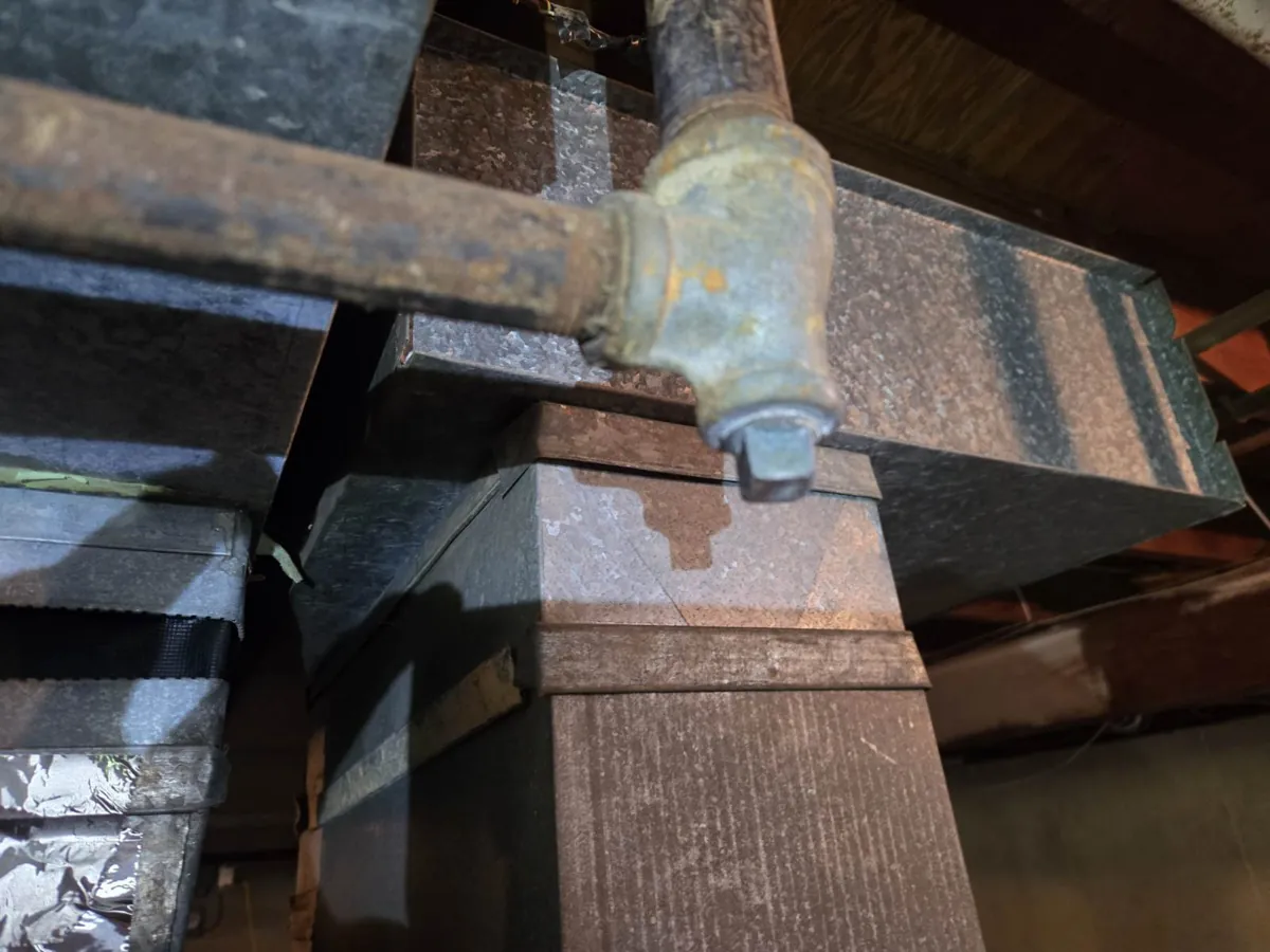 Old rusted pipe and a capped fitting next to basement ductwork