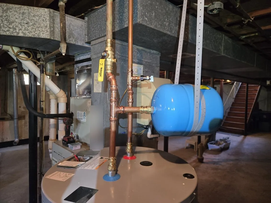 New copper piping on top of the water heater with a yellow-handled ball valve and a blue expansion tank held by strapping