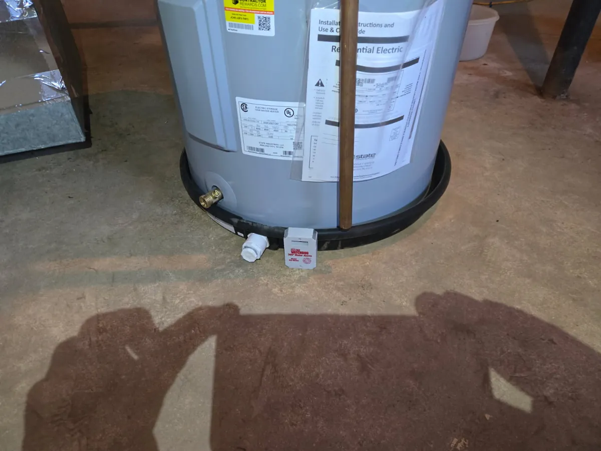 Base of the new electric water heater in a black drip pan with a drain valve and a water leak alarm on the floor