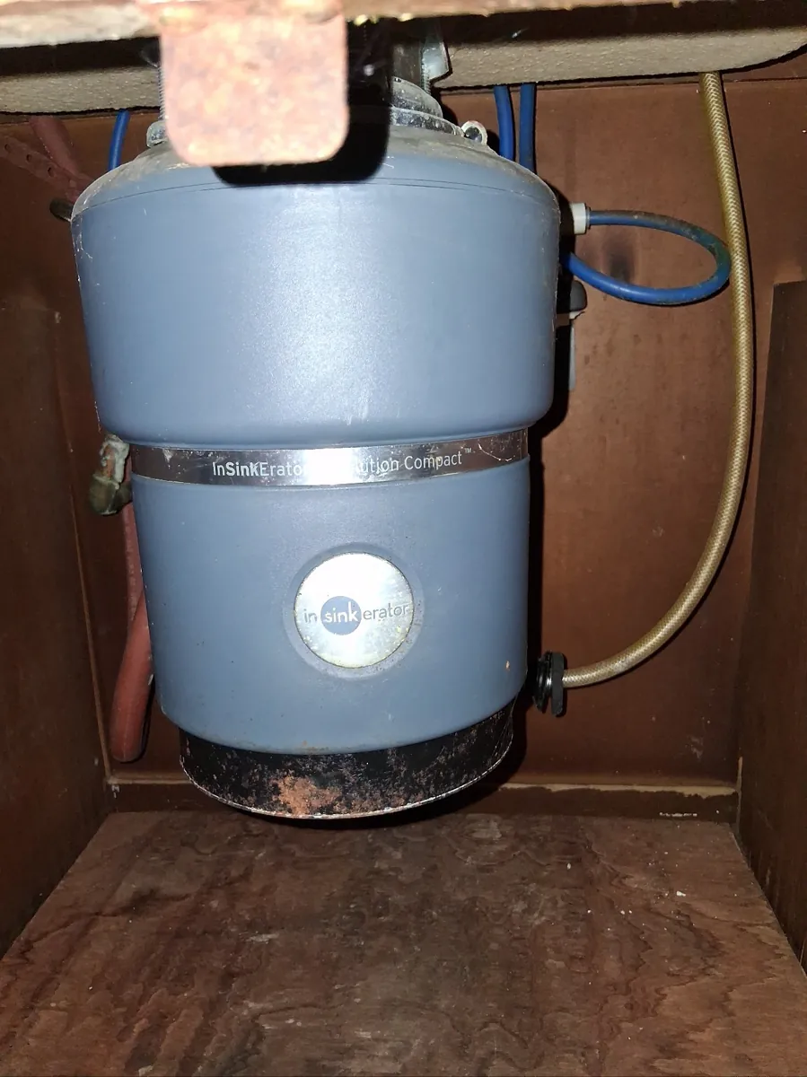Old gray InSinkErator garbage disposal with a rusted bottom under a kitchen sink