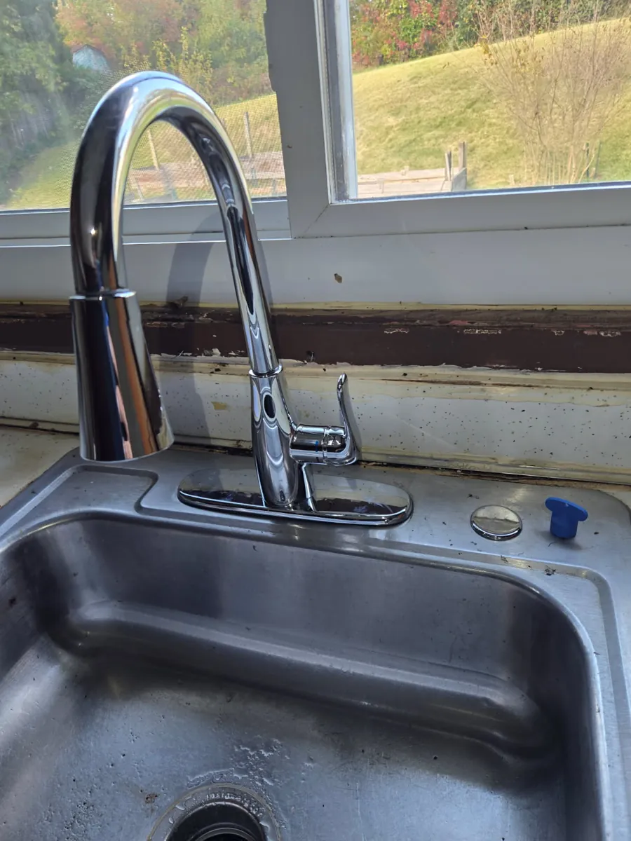 New chrome single-handle pull-down kitchen faucet on a stainless steel sink in front of a window