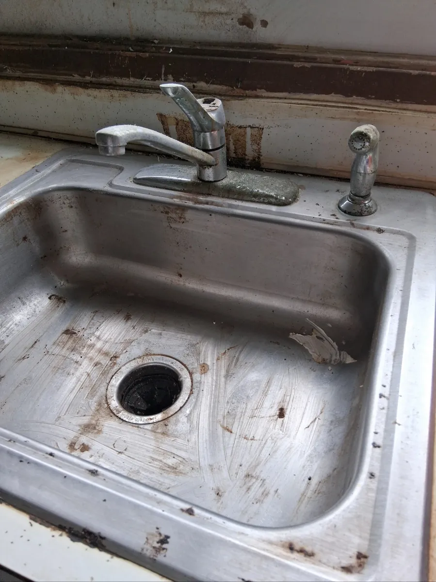 Old worn single-handle kitchen faucet with a separate side sprayer on a stainless steel sink