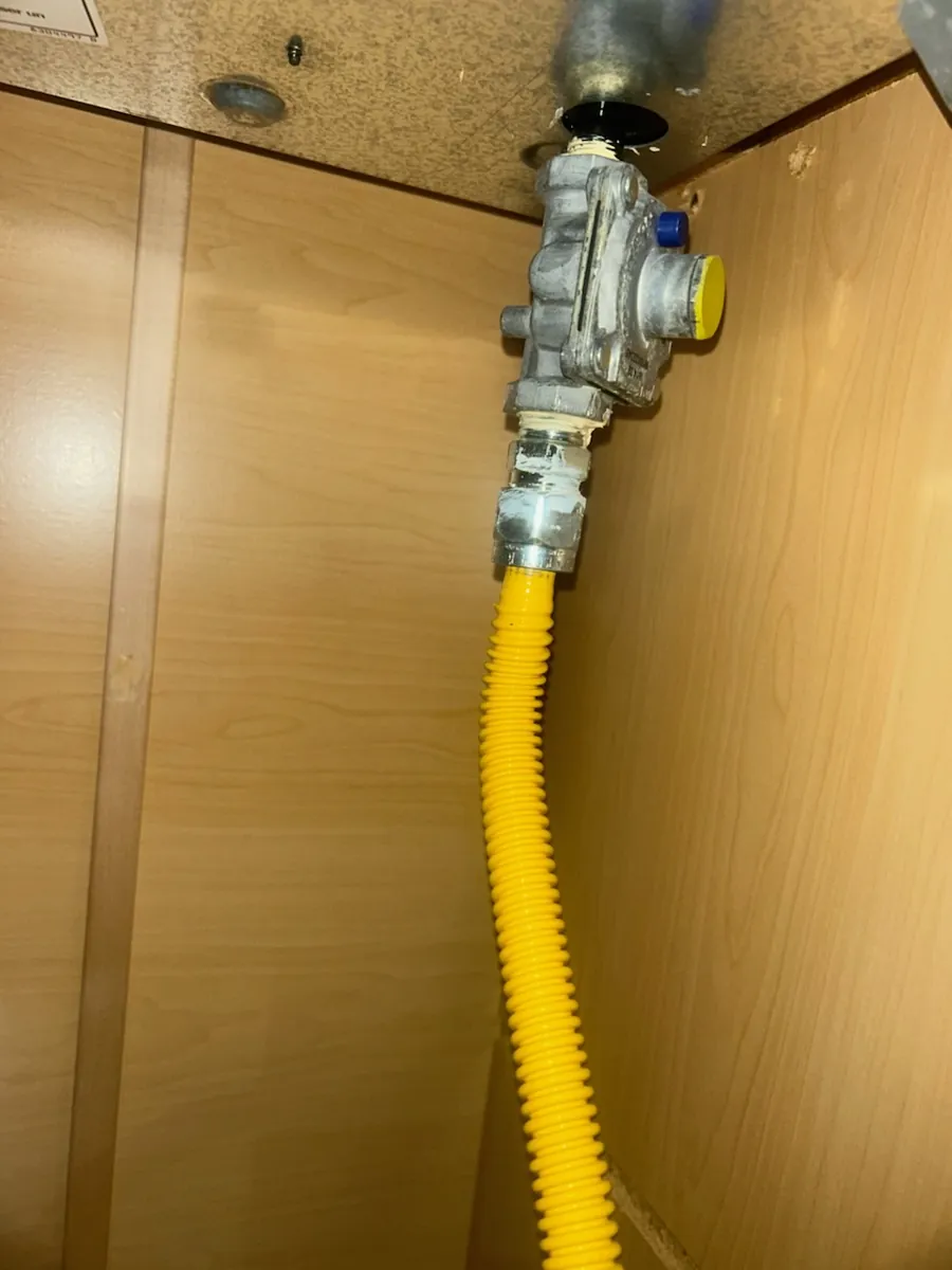 Yellow coated flexible gas connector running up to a gas fitting inside a wood cabinet