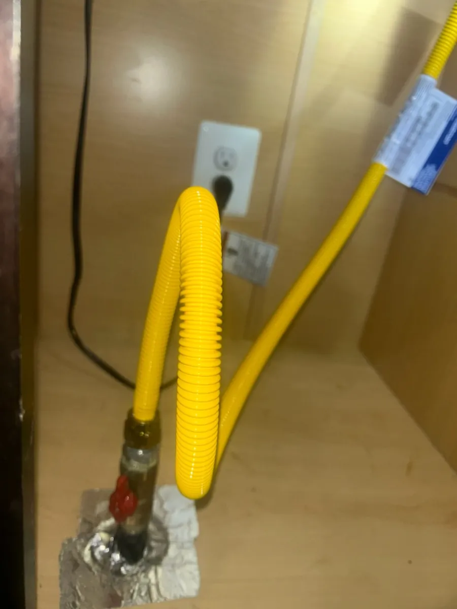 New yellow flexible gas connector looping up from a red-handled shutoff valve at the cabinet floor