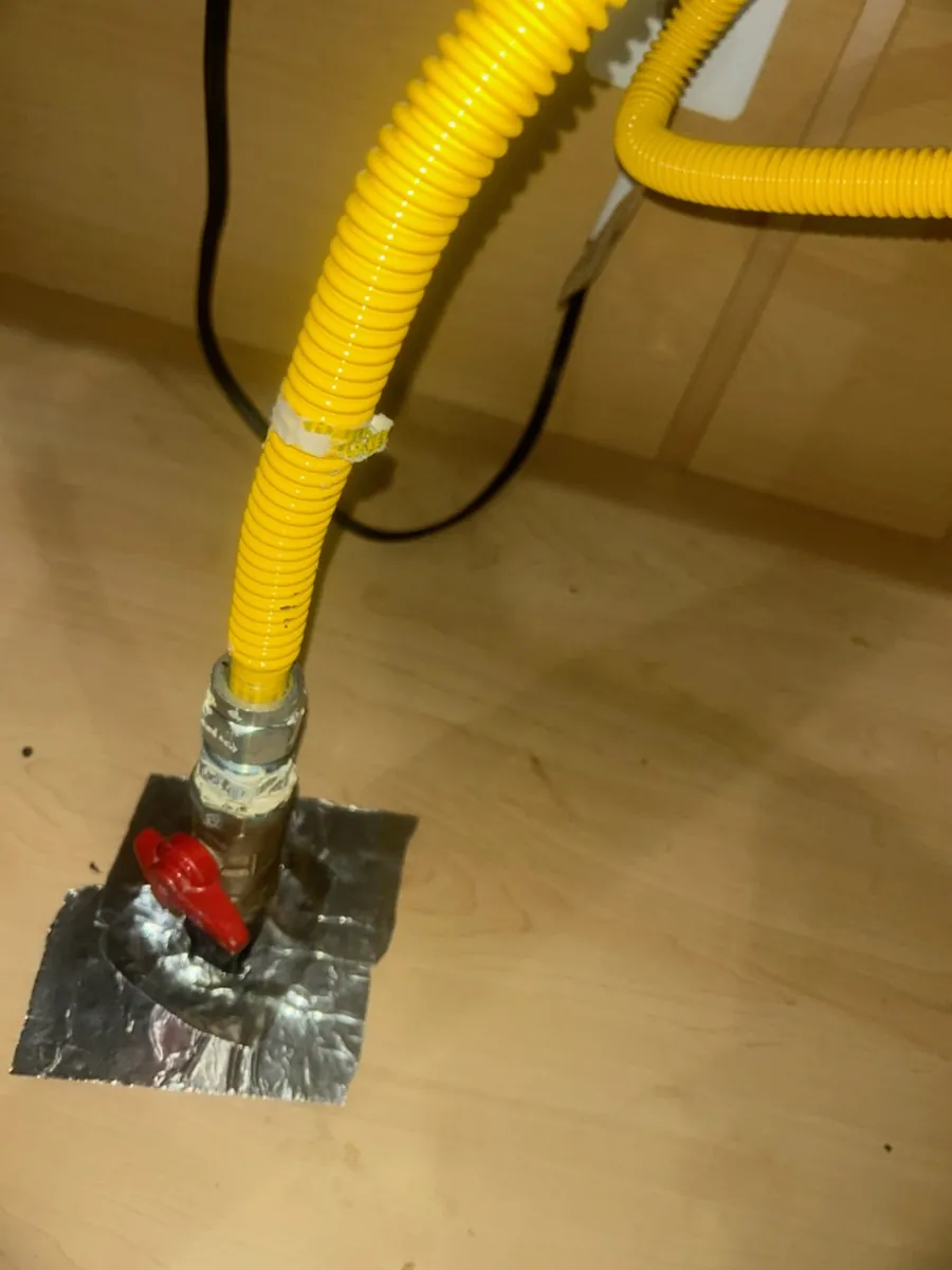 Close-up of a gas shutoff valve at the floor with a yellow flexible connector attached
