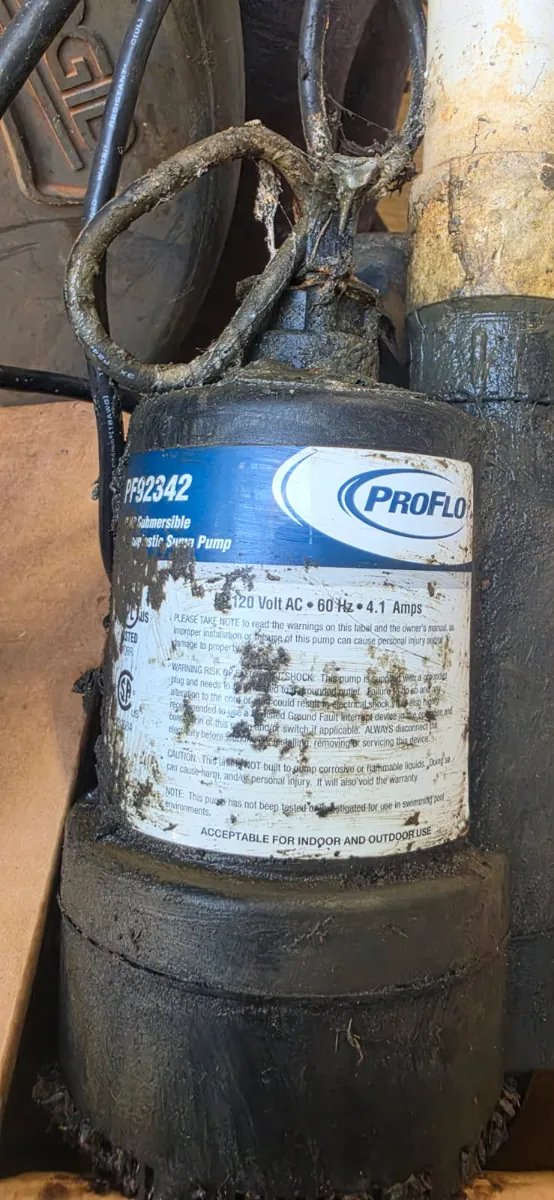 Old ProFlo PF92342 thermoplastic sump pump pulled from the pit, caked in sludge, with its cord wrapped around the handle