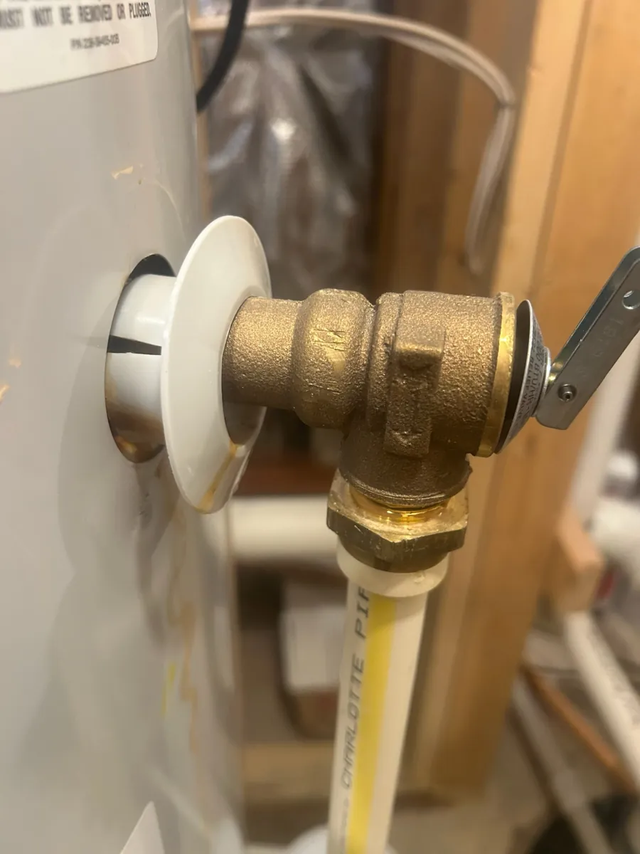 Brass temperature and pressure relief valve on a water heater, with a white discharge pipe running down