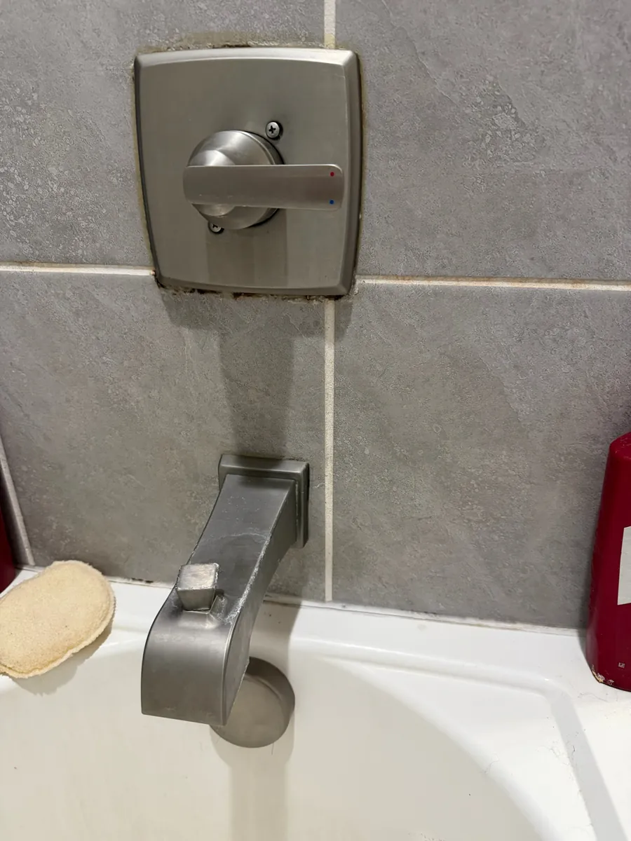 Brushed nickel single-handle tub and shower valve trim above a tub spout with a pull-up diverter on gray tile