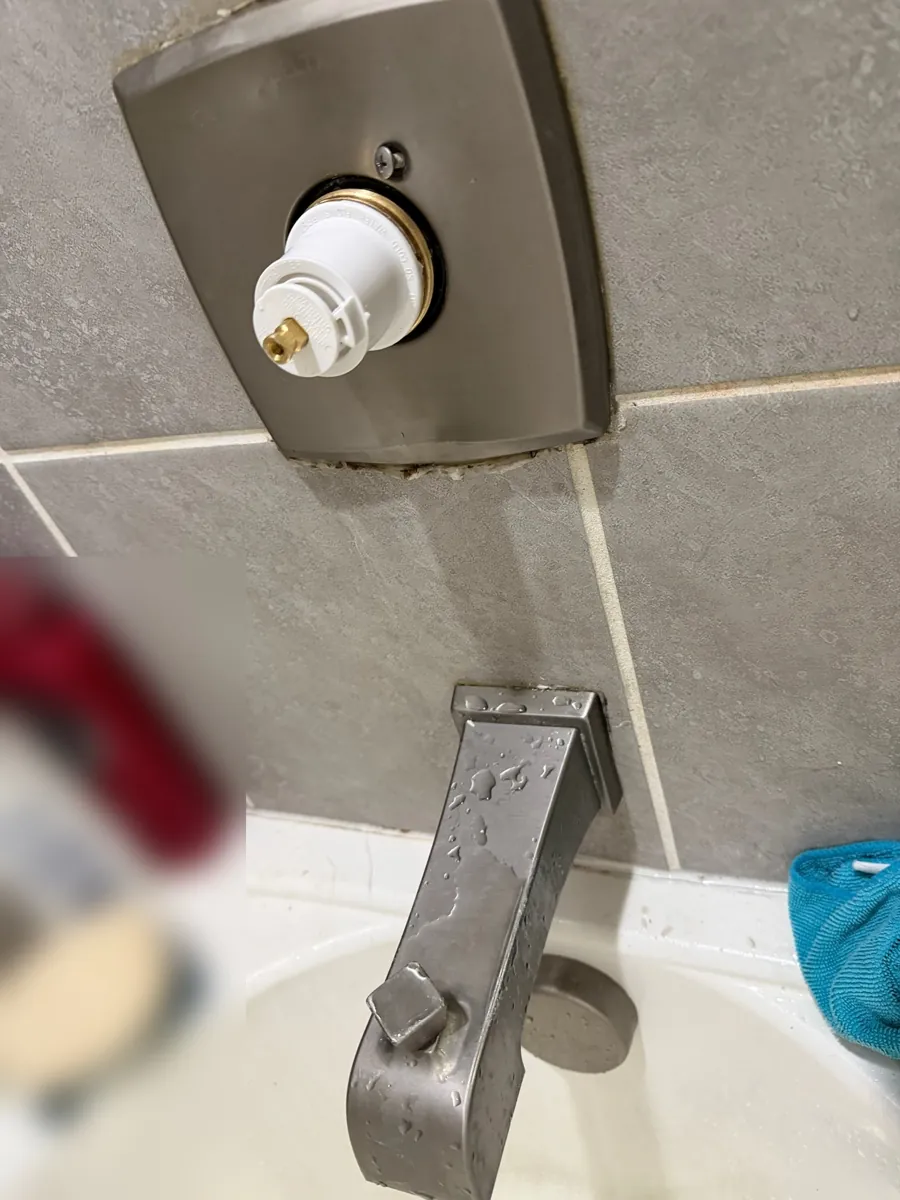 New white valve cartridge seated in the tub valve with the handle removed, above a brushed nickel tub spout