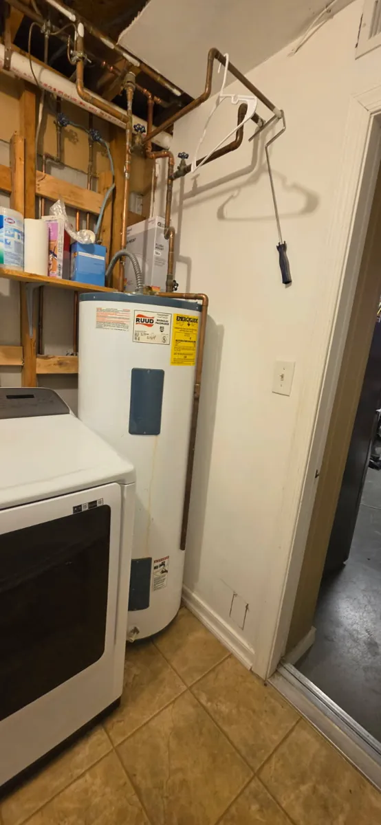 Wider view of the old electric water heater in the laundry room corner