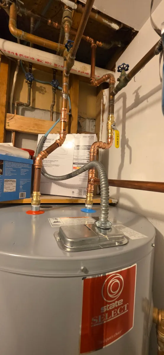 Top of the new water heater showing new copper pipe, a yellow-handled ball valve and flexible electrical conduit