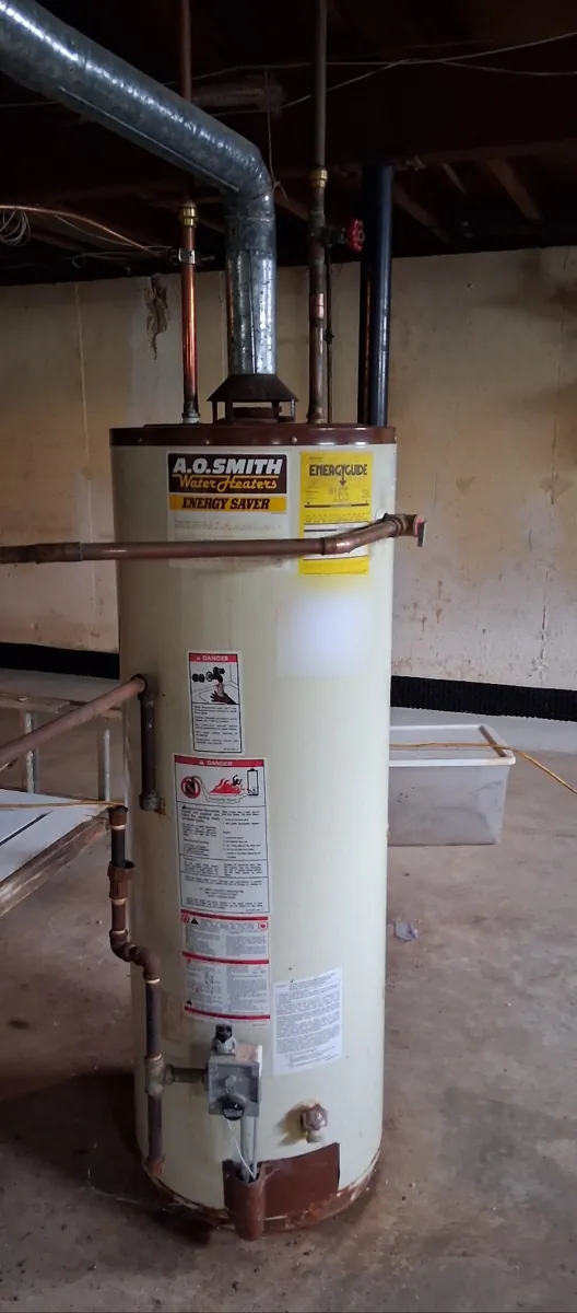 Older A.O. Smith gas tank water heater in an unfinished basement with a metal flue pipe