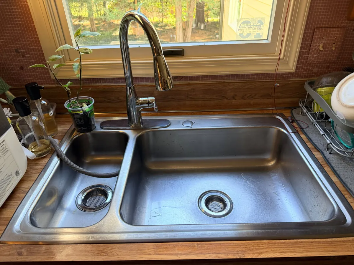 Wider view of the double-bowl stainless kitchen sink and countertop under a window
