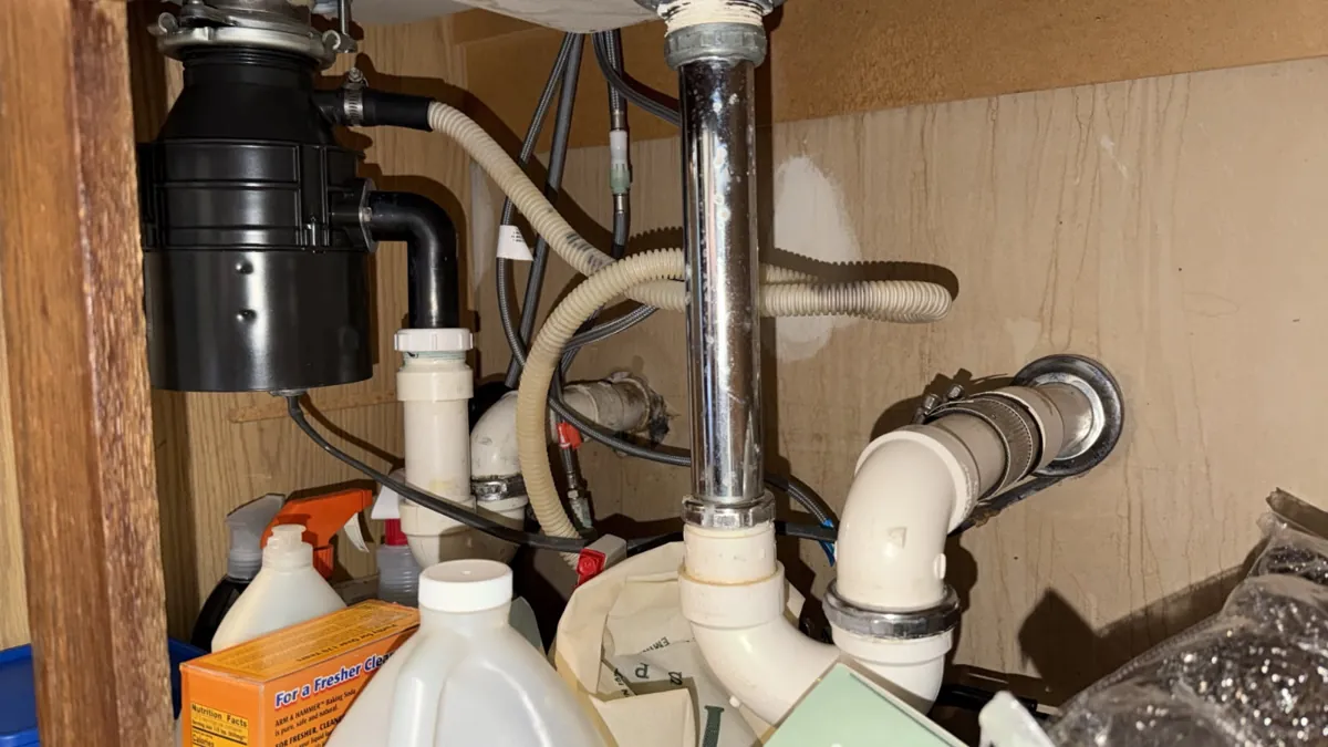 Garbage disposal with a corrugated drain hose connected to its side, plus white PVC trap and chrome tailpiece